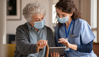 Mature woman with doctor wearing surgical mask and using digital tablet during coronavirus pandemic.